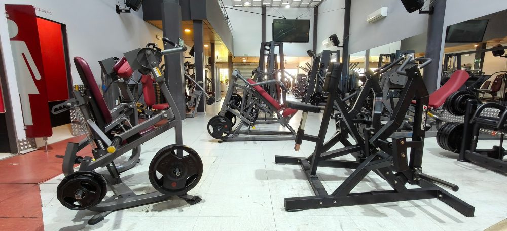 Gimnasio con varios equipos de ejercicio y pesas en un ambiente moderno.