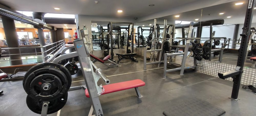 Gimnasio con equipos de pesas y máquinas de ejercicio en un ambiente luminoso.