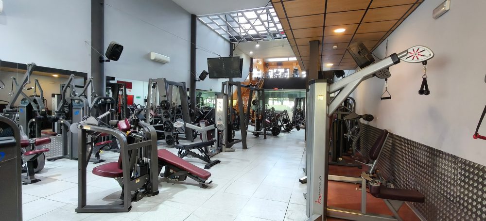 Gimnasio moderno con equipos de ejercicio y áreas de entrenamiento.
