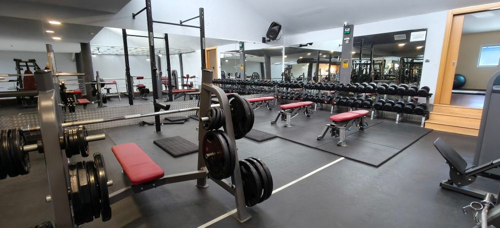 Gimnasio con pesas, bancos y máquinas de ejercicio en un espacio iluminado.